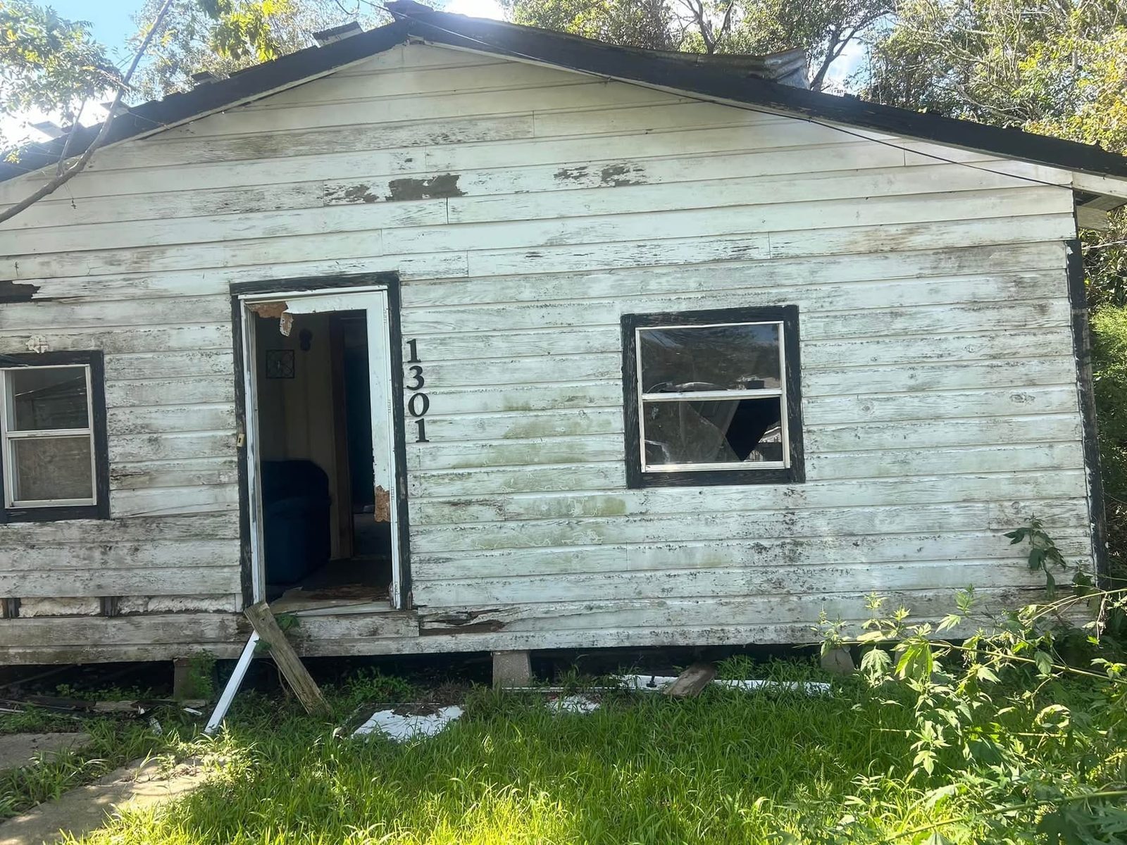 Before demolition: a run-down white wood house with peeling paint, a broken window and no front door