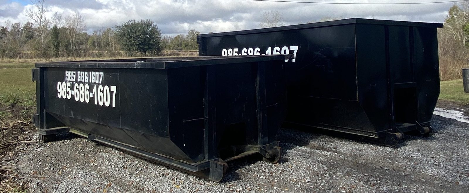 Two black Trash King roll-off dumpsters side by side on gravel, a low one and a taller one, each with 985-686-1607 on the side