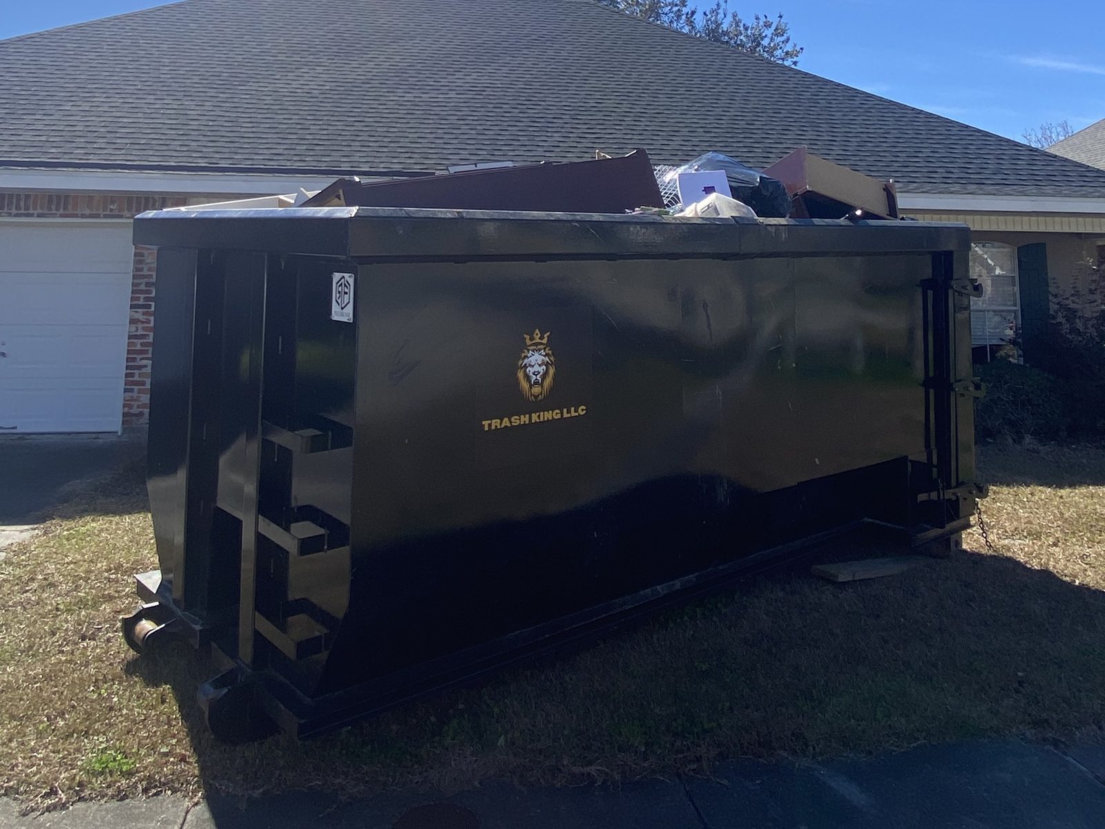 A Trash King dumpster filled with household items in front of a brick home